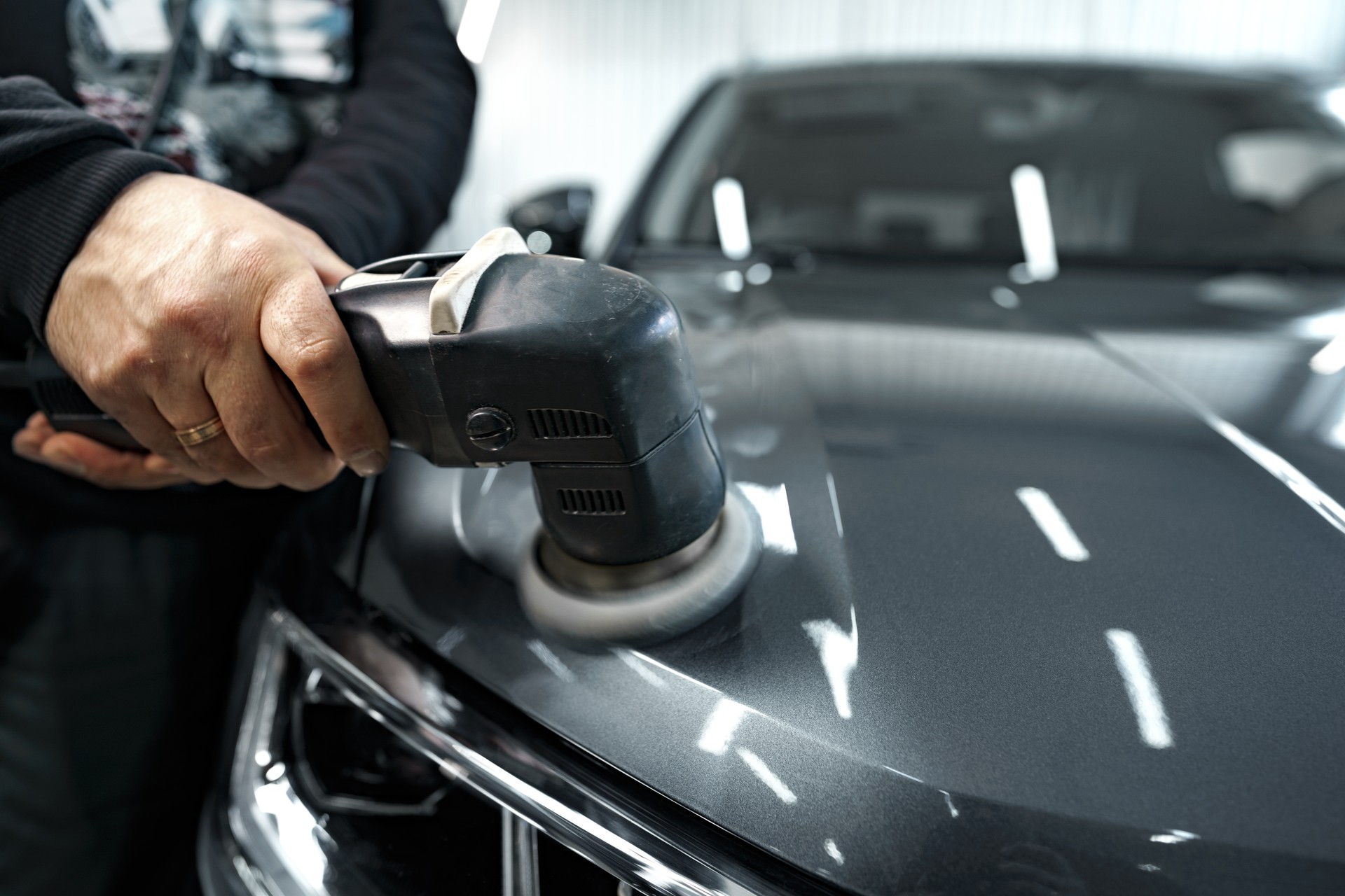 Car detailing. Male hands with orbital polisher in auto repair shop